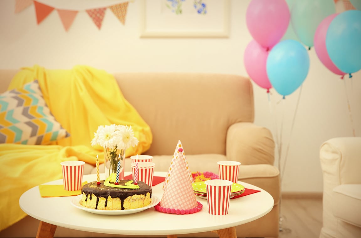 a kids birthday party table with cake, balloons, party hats, paper cups and decorations on the wall. 